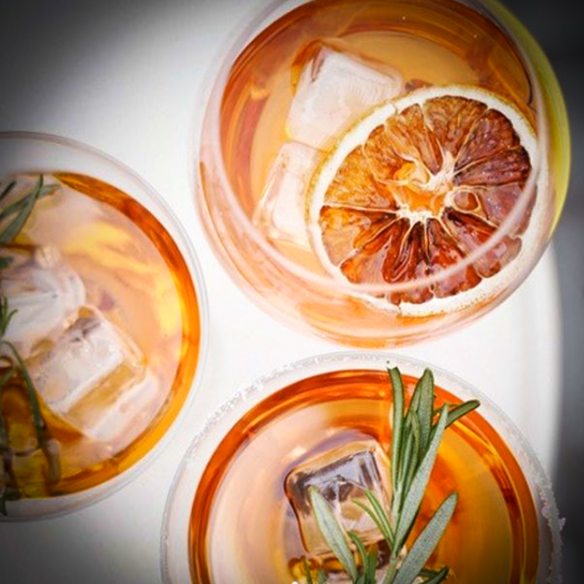 Trois cocktails ambrés préparés en quantité avec agrumes et romarin